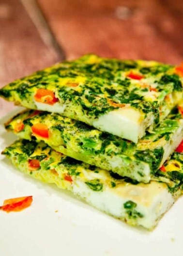A stack of spinach and red pepper frittata slices on a wooden surface.