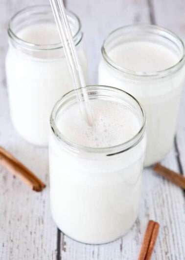 Three jars of milk with a straw in one and cinnamon sticks alongside.