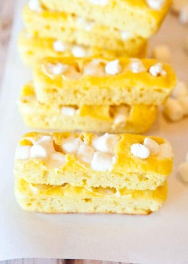Slices of homemade rice krispie treats with marshmallow pieces on a parchment paper.