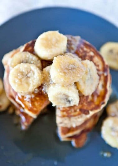 Stack of pancakes with banana slices and syrup on a dark plate.