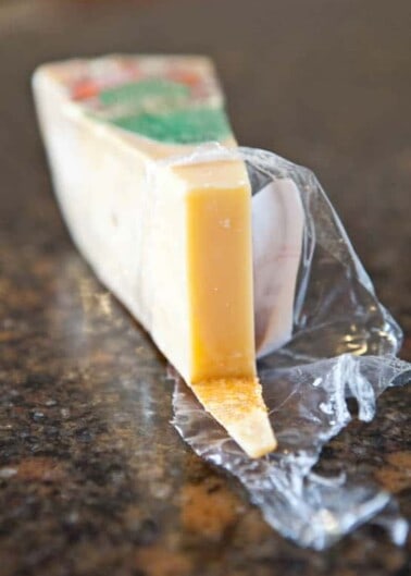A wedge of parmesan cheese partially wrapped in plastic on a countertop.