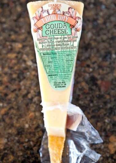 A tube of trader joe's aged gouda cheese with a piece sliced off.