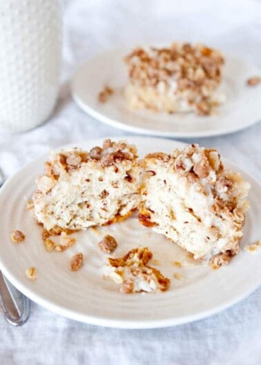 A slice of coffee cake with streusel topping served on a white plate with a glass of milk in the background.