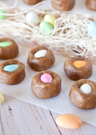 Homemade easter-themed treats with colorful candy eggs nestled in dough nests on a wooden surface.