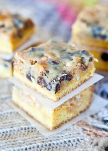 Stack of homemade blondies with chocolate chips and nuts on a lace tablecloth.