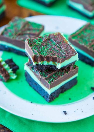 Layered mint chocolate brownies with a green sprinkled topping served on a white plate.