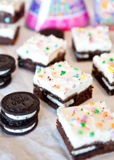 Chocolate brownies topped with cream and colorful sprinkles, accompanied by sandwich cookies.