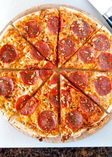A pepperoni pizza with a slice missing, on a white surface.