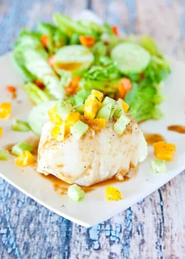 Grilled fish topped with diced mango served with a side of salad on a white plate.