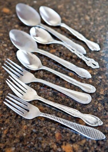 A set of forks and spoons with decorative handles arrayed on a countertop.