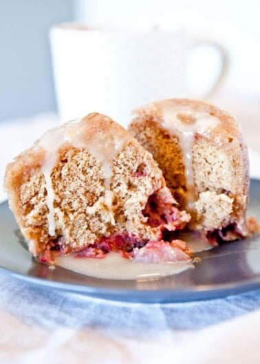 A sliced muffin with visible berries on a plate, drizzled with icing, beside a mug.