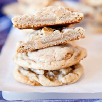 Freshly baked cookies stacked on a white surface with one cookie broken in half to show the inside.