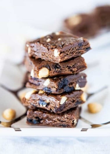 A stack of chocolate brownies with nuts on a white surface.