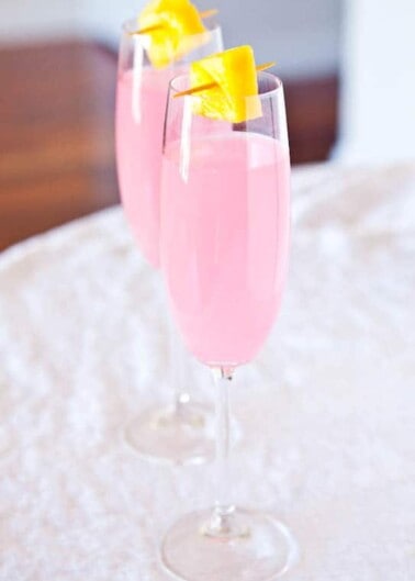 Two glasses of pink beverage garnished with orange slices on a white cloth.