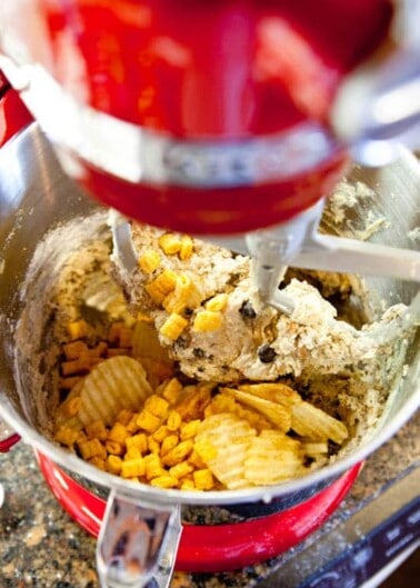 Mixing cookie dough with chips and cereal in a red stand mixer.