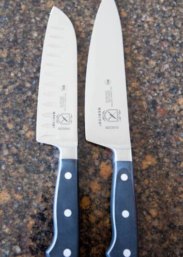 Two chef's knives with black handles on a countertop.