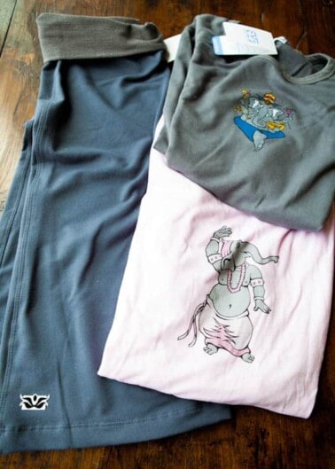 A pair of gray pants next to two folded t-shirts, one gray with a duck graphic and one pink with an elephant graphic, laid out on a wooden surface.