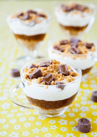 Layered dessert in glass cups with crumbled biscuits and chocolate pieces on top.