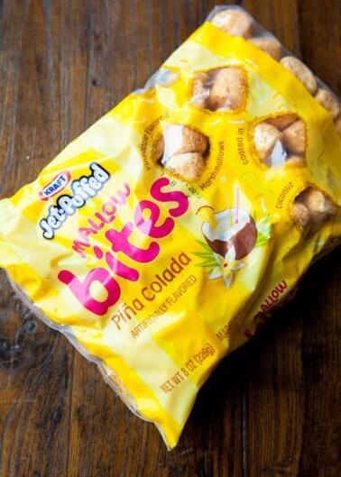 An opened package of jet-puffed mallow bites with pina colada flavor on a wooden surface.