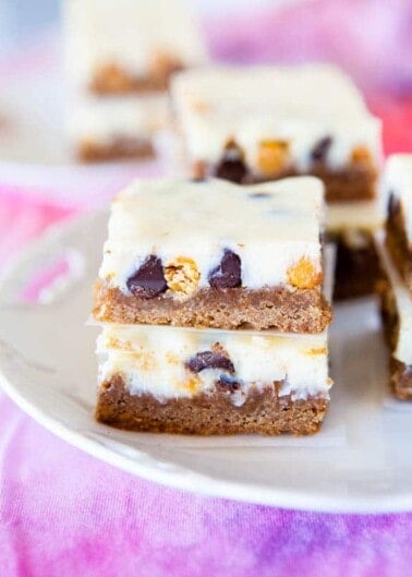Plate of layered dessert bars with chocolate chips and a creamy topping.