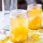 A mason jar filled with a peach-infused beverage on a table with a floral cloth.