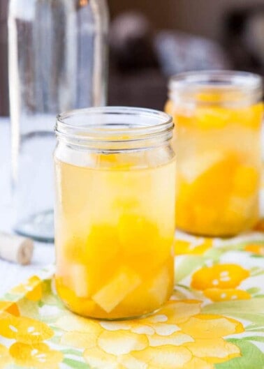 A mason jar filled with a peach-infused beverage on a table with a floral cloth.