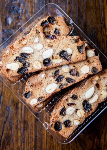 Slices of biscotti with almonds and dried fruit in a plastic container.