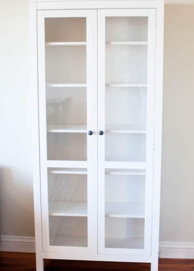 White cabinet with glass doors against a plain wall.