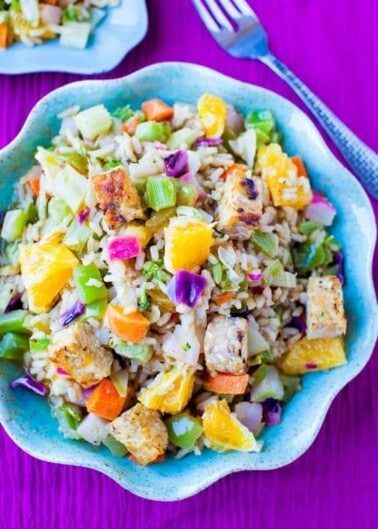 A colorful bowl of salad with grilled chicken, various fruits, and vegetables on a purple background.
