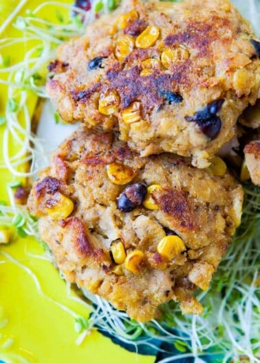 A stack of corn and bean fritters on a bed of sprouts.