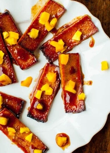 Glazed tofu slices topped with diced mango on a white plate.