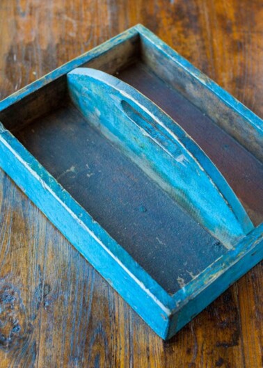 A worn blue wooden tray with a boat-shaped indentation on a wooden surface.