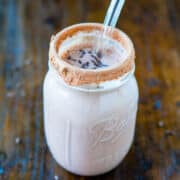 Mason jar filled with a chocolate milkshake and a metal straw, with a cocoa powder rim, on a wooden surface.