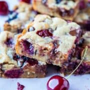 Squares of cherry and berry-filled dessert bars on a white surface.