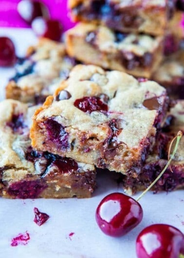 Squares of cherry and berry-filled dessert bars on a white surface.