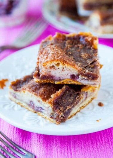 A stack of cinnamon swirl cheesecake bars on a white plate with a pink background.