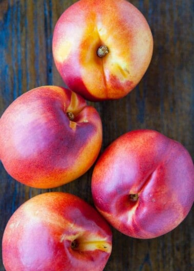 Four ripe peaches on a wooden surface.