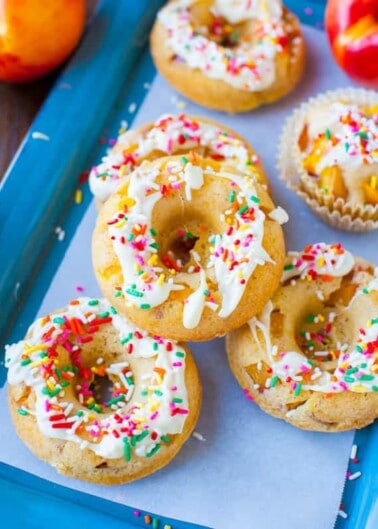 Six baked doughnuts with white icing and colorful sprinkles on a blue tray.