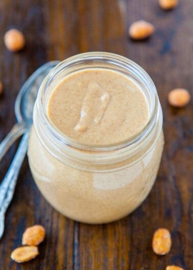 A jar of creamy peanut butter with peanuts on a wooden table.