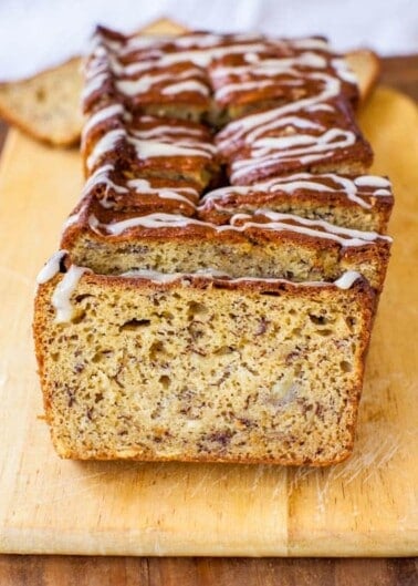 Sliced banana bread with icing drizzle on a wooden board.