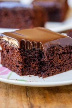 A slice of homemade chocolate ganache cake on a plate missing a bite.