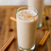 A glass of cinnamon-spiced smoothie on a wooden surface with cinnamon sticks nearby.