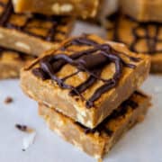 Stacked peanut butter bars with chocolate drizzle on parchment paper.