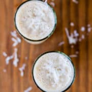 Two glasses of coconut smoothie viewed from above on a wooden surface with coconut shavings scattered around.