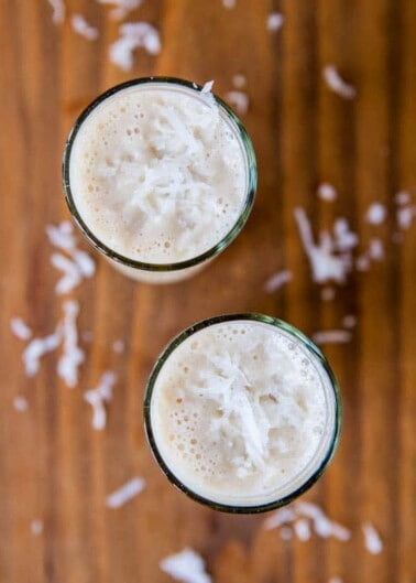 Two glasses of coconut smoothie viewed from above on a wooden surface with coconut shavings scattered around.
