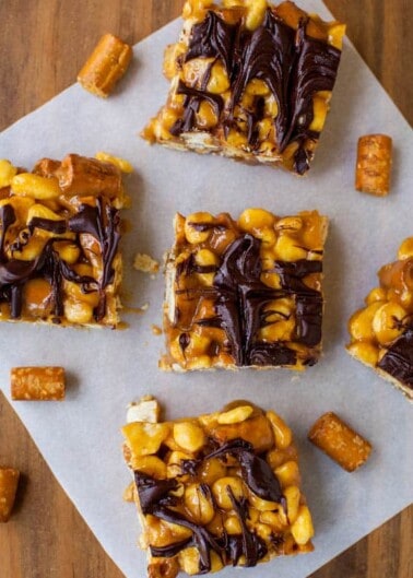 Caramel peanut chocolate bars on parchment paper with caramel pieces around them.