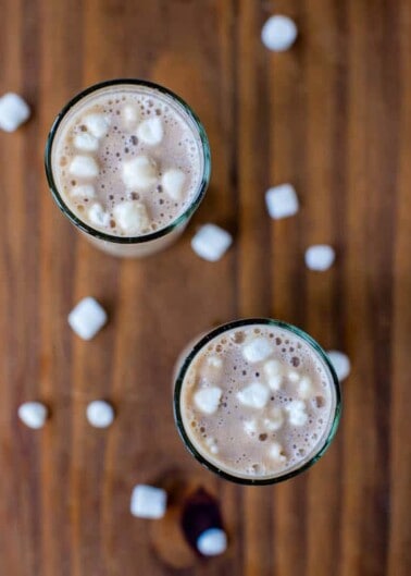 Two glasses of hot chocolate with marshmallows on a wooden surface.