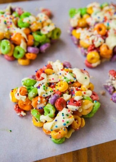 Colorful cereal treats with white icing and sprinkles on parchment paper.