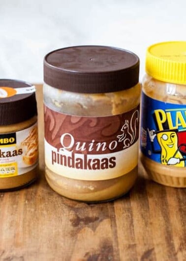 A variety of peanut butter brands lined up on a wooden surface.