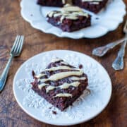 A slice of chocolate cake with white icing drizzle on a decorative white plate, with more pieces in the background.